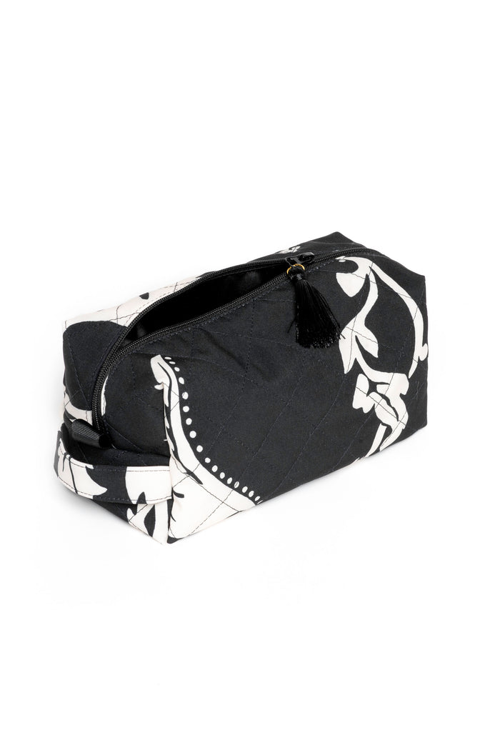 Small black makeup pouch with white floral print opened to reveal black lining and compact storage for beauty essentials