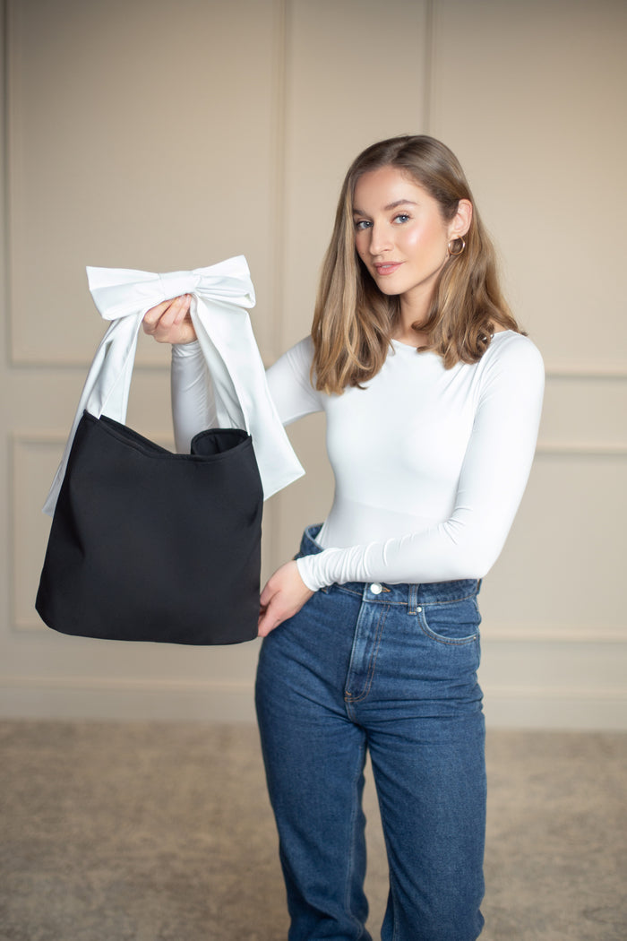 Elegant black tote bag featuring a contrasting white strap and feminine bow, a timeless accessory for daily use or professional looks.