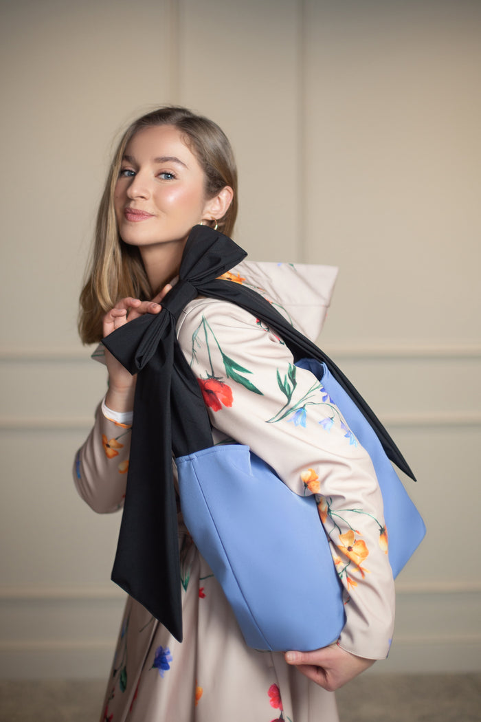 Elegant blue tote bag with black bow-accented strap, designed to complement RainSisters coats.