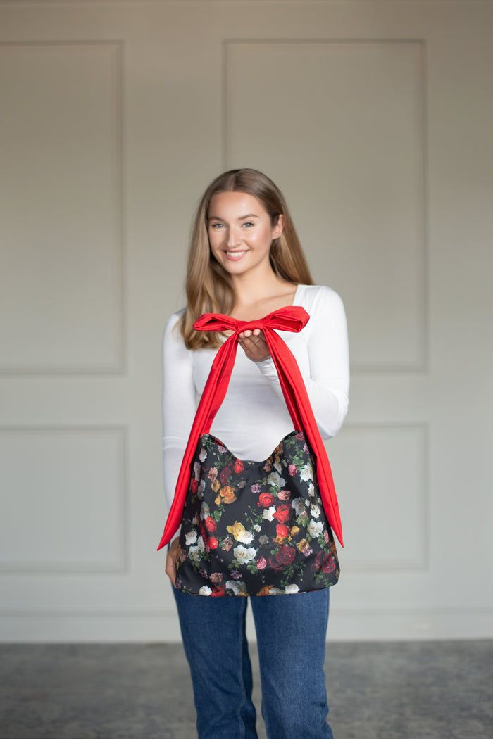 Close-up of the red bow strap tied across the black tote bag with vibrant floral pattern.