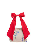 Beige handbag with floral print and a bold red bow on a white background