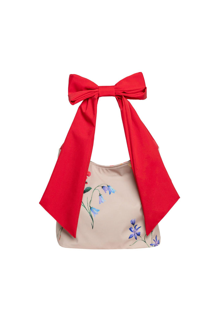 Beige handbag with floral print and a bold red bow on a white background