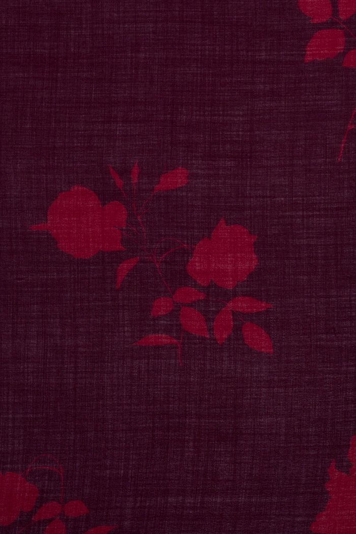 A close-up of dark burgundy fabric with a subtle woven texture and a tonal red rose floral pattern.