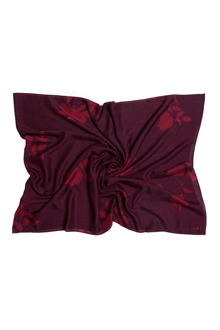 A dark plum purple scarf with a subtle tonal floral pattern, styled in a central twist on a plain white background.