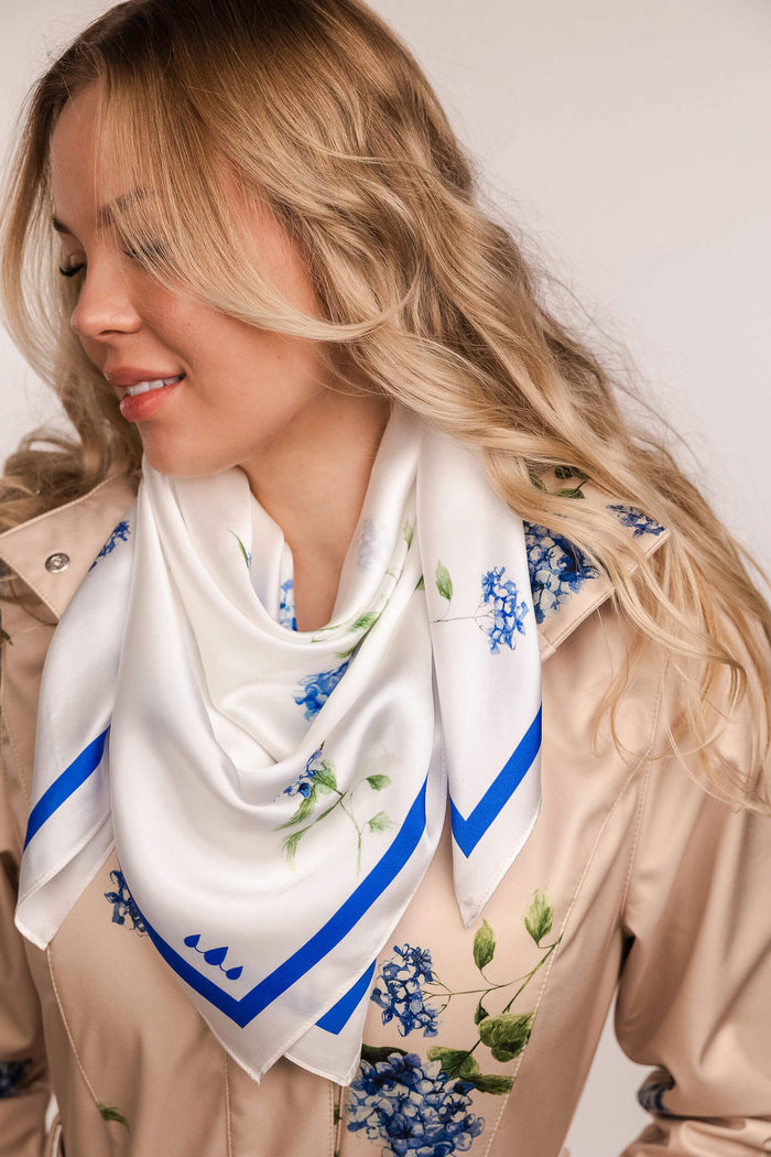 Woman wearing a white scarf with blue floral patterns on a plain background