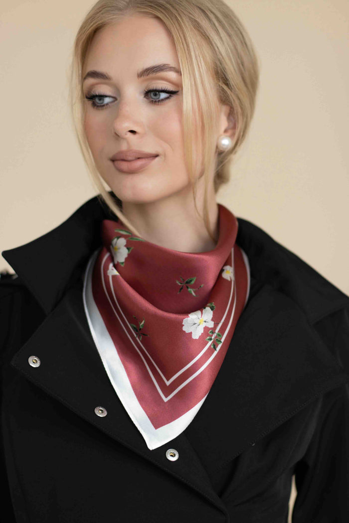 Woman wearing a red floral scarf with a black coat against a beige background